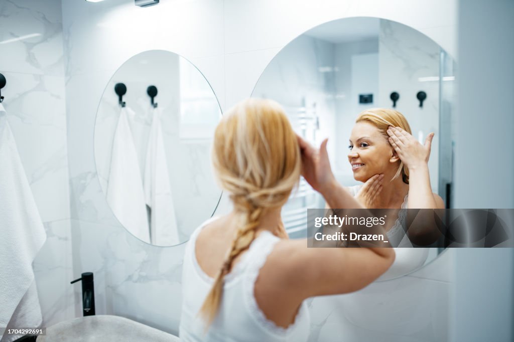 Aging woman in front of the mirror looking at wrinkles and smiling