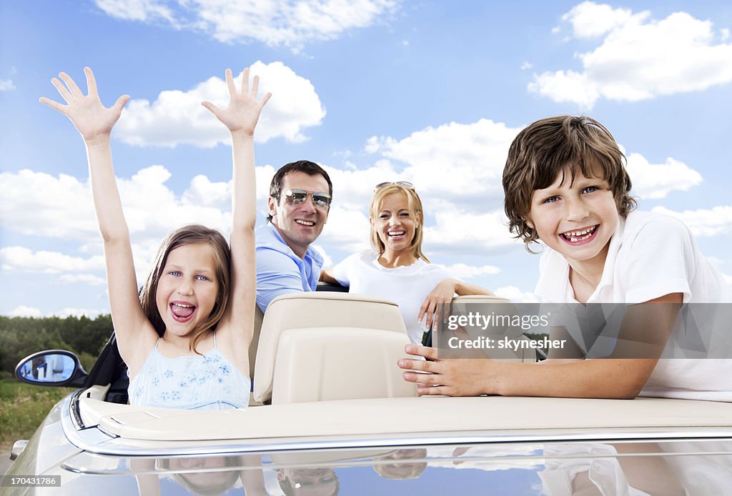 Happy family in cabriolet against the blue sky.