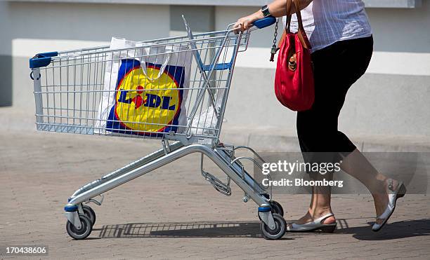 Customer uses a shopping cart to move her purchases across the parking lot outside a Lidl discount supermarket store, operated by Schwarz Group, in...