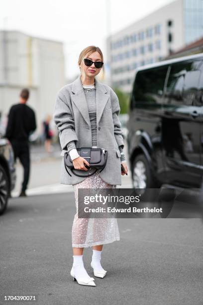 Guest wears sunglasses, necklaces, a grey pullover, a grey fluffy jacket, a two-tone Prada bag, a sequined white transparent lace midi skirt, white...