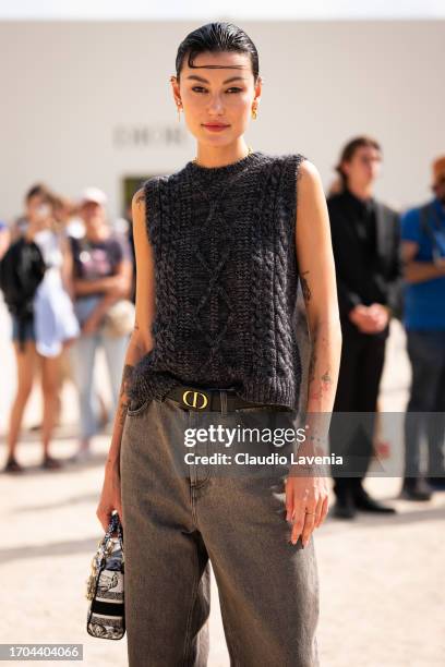 Amalie Gassmann wears a grey knitted vest, grey jeans, Dior belt and Dior printed bag, outside Dior, during the Womenswear Spring/Summer 2024 as part...