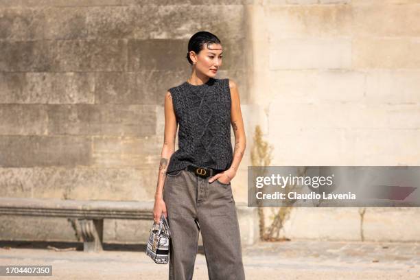 Amalie Gassmann wears a grey knitted vest, grey jeans, Dior belt and Dior printed bag, outside Dior, during the Womenswear Spring/Summer 2024 as part...