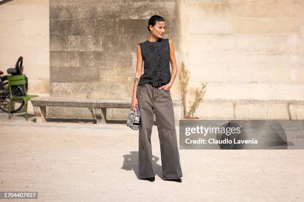 Amalie Gassmann wears a grey knitted vest, grey jeans, Dior belt, black heels and Dior printed bag, outside Dior, during the Womenswear Spring/Summer...