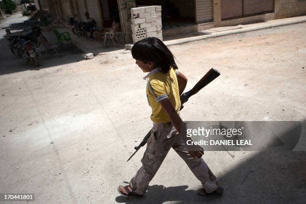 Syrian young boy walks holding an old rifle as he helps fighters belonging to the "Martyrs of Maaret al-Numan" battalion on June 13, 2013 in the...