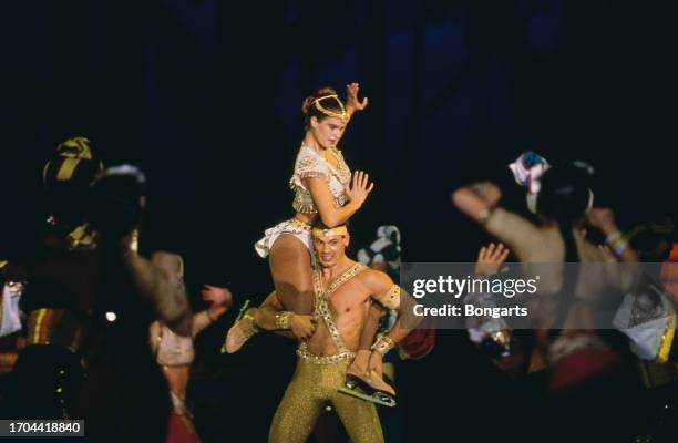 German figure skater Katarina Witt sitting on male dancer's shoulders as they perform a routine on the ice during a 'Holiday on Ice' show, held at...