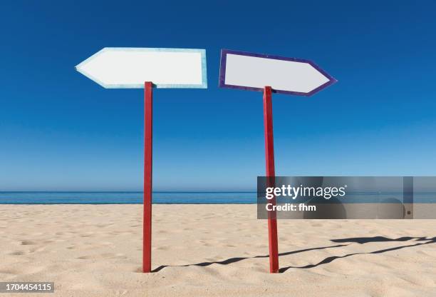 two arrow signs in the opposite direction on the beach - stakes in the sand stock pictures, royalty-free photos & images