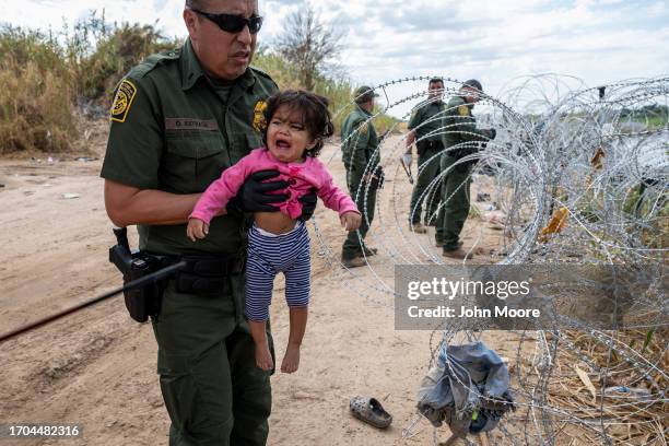 Border Patrol agent holds Melanie Moran from Venezuela as her parents cross through razor wire at the U.S.-Mexico border on September 27, 2023 in...