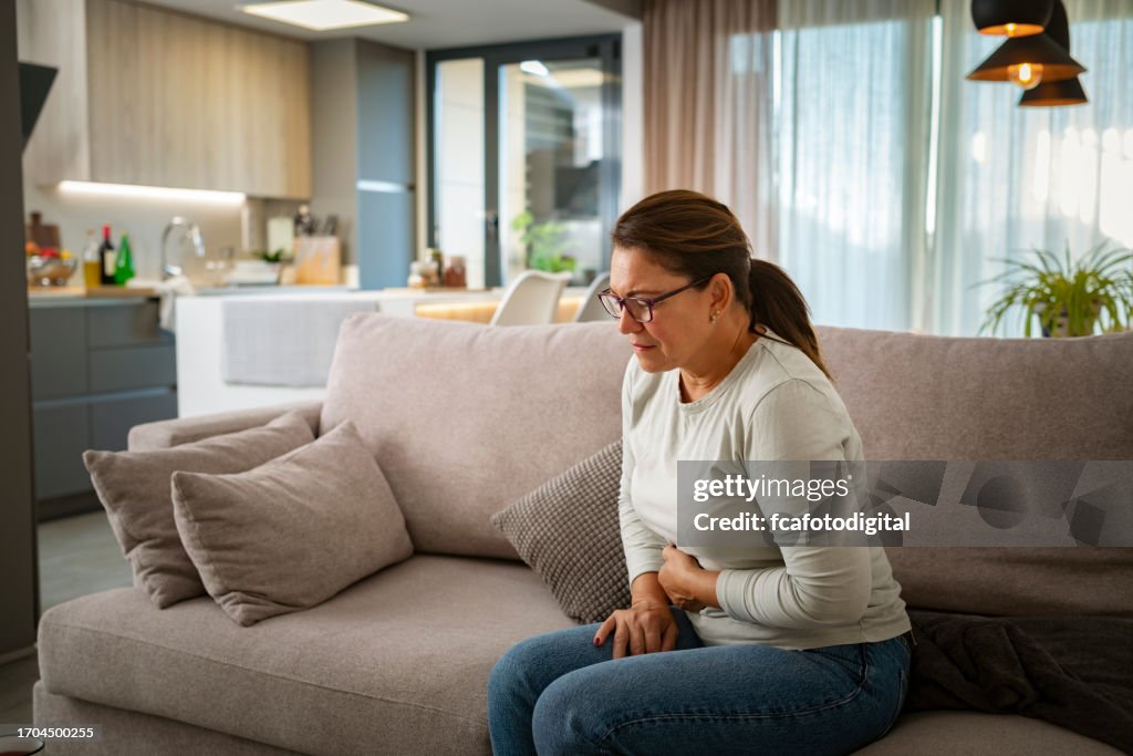 Ungesunde reife Frau mit Bauchschmerzen sitzt auf der Couch