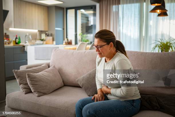 donna matura malsana con mal di stomaco seduta sul divano - kidney stone foto e immagini stock