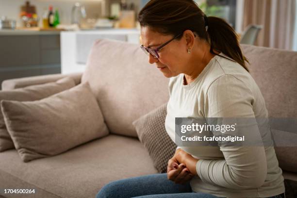 mulher que sofre de cólicas estomacais no sofá em casa - apendicite - fotografias e filmes do acervo