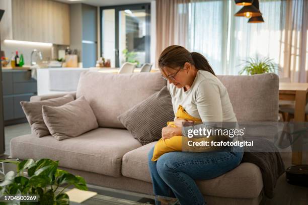 unhealthy mature woman with stomachache sitting on the couch - woman crotch stock pictures, royalty-free photos & images