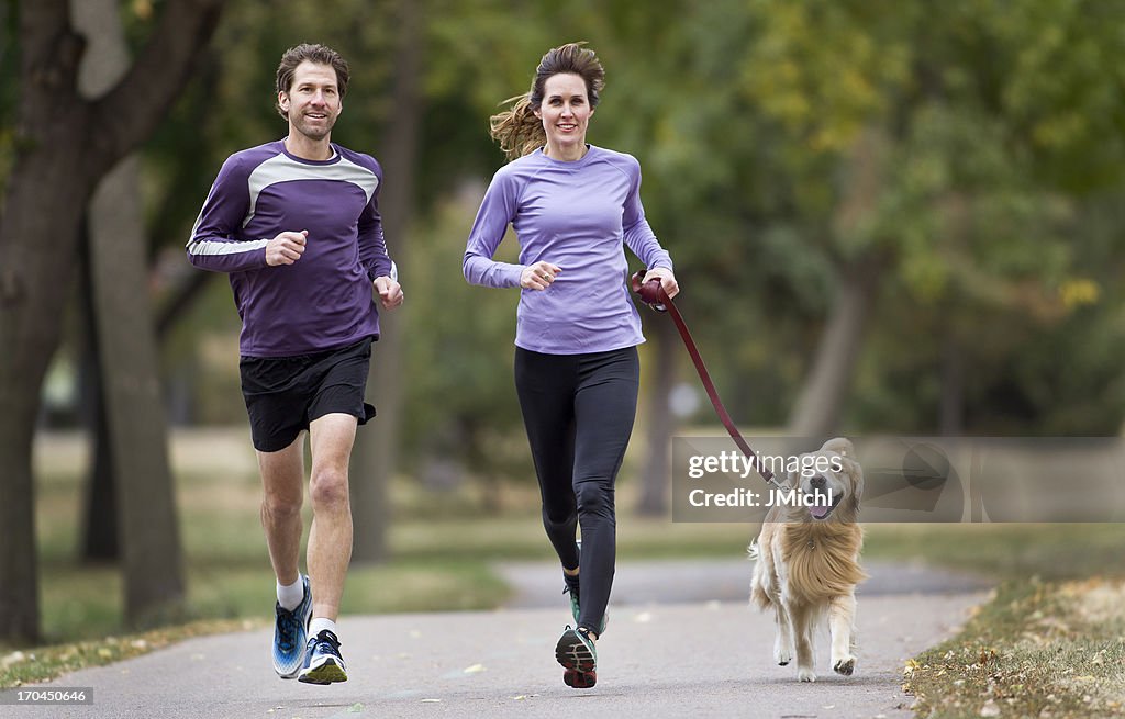 A couple jogging in the park with their golden retriever