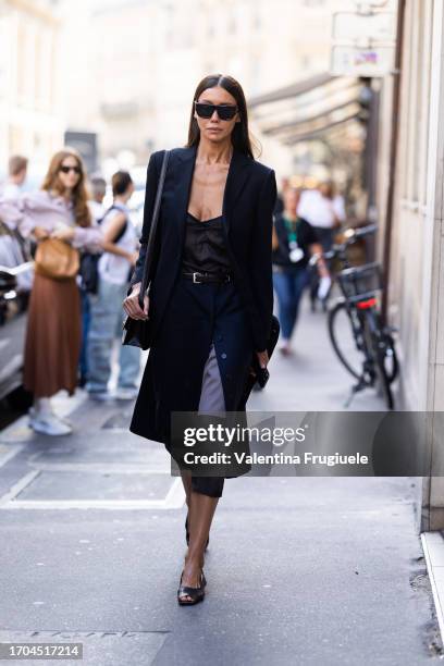 Guest is seen wearing black Gucci sunglasses, a blue jacket, a black tank top, a blue midi skirt open in the front with lilac and brown layers, a...