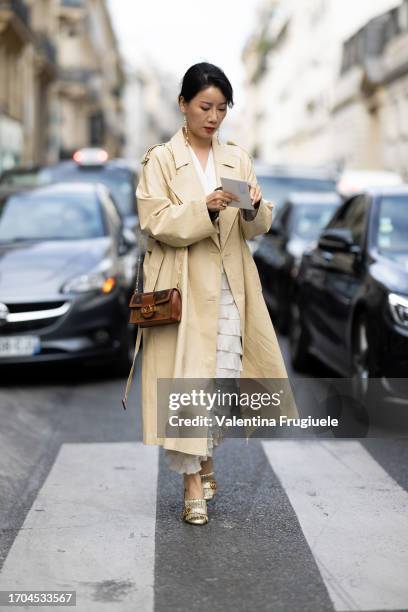 Guest is seen wearing a cream trench coat over a white dress outside Dries Van Noten show during the Womenswear Spring/Summer 2024 as part of Paris...