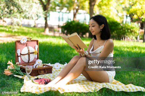asian woman reading a book during a picnic in a park - picnic blanket stock pictures, royalty-free photos & images