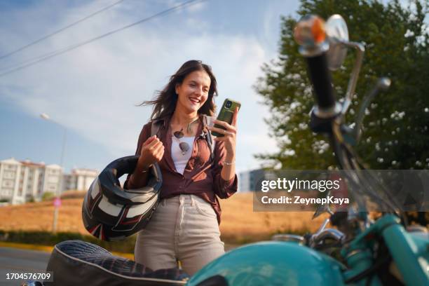giovane conducente femminile che utilizza il telefono cellulare accanto alla sua moto. - motocicletta foto e immagini stock