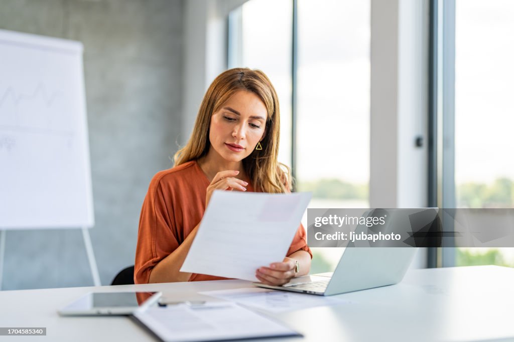 Giovane donna d'affari felice e di successo che lavora con i documenti all'interno dell'ufficio.