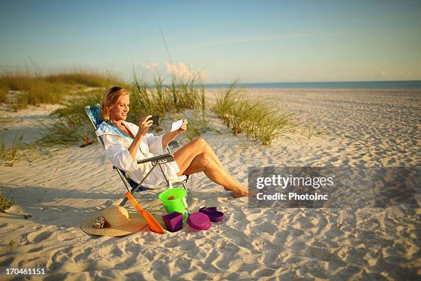 mature woman at the beach depositing a check with phone - cheque deposit stock pictures, royalty-free photos & images