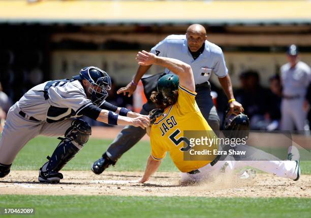 John Jaso of the Oakland Athletics slides safely under the tag of Chris Stewart of the New York Yankees to score on a hit by Seth Smith of the...