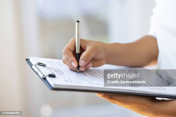 holding clipboard and a pen in office - woman filling out paperwork stockfoto's en -beelden