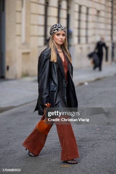 Joicy Muniz wears head scarf, black oversized leather jacket, brown Alaia heart bag, flared rust brown pants, necklace during the Womenswear...