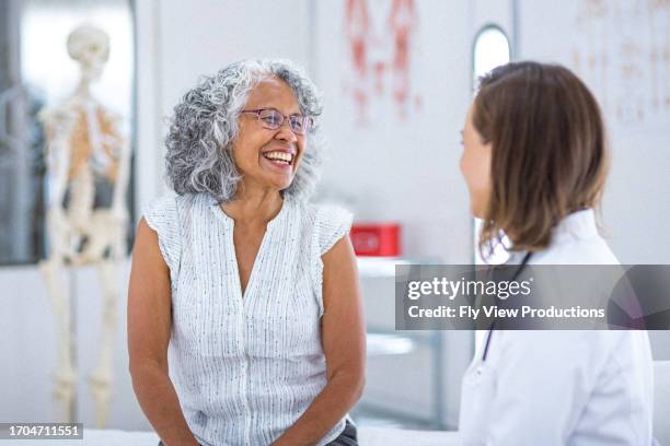 healthy senior woman talking with her doctor - dokterspraktijk stockfoto's en -beelden