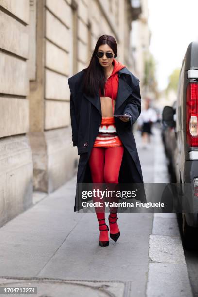 Guest is seen wearing black sunglasses, black leather heels, a black Nike long trench, red tights, a red skirt with a mouth printed on and a red...