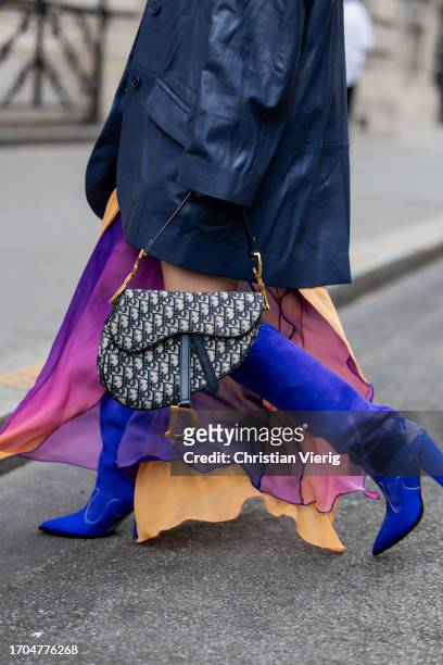 Joicy Muniz wears Dior bag, blue knee high cowboy boots, oversized navy blazer, purple orange asymmetric transparent dress, cat eye sunglasses,...