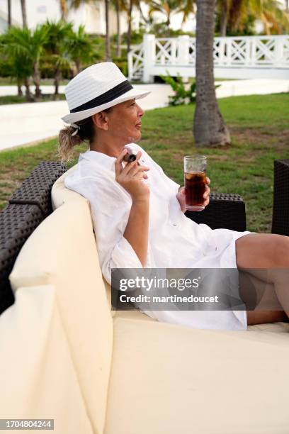 hermosa mujer 50+ fumando un cigarro en un entorno tropical. - beautiful women smoking cigars fotografías e imágenes de stock