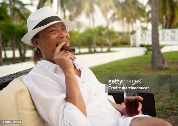 hermosa mujer 50+ fumando un cigarro en un entorno tropical. - beautiful women smoking cigars fotografías e imágenes de stock