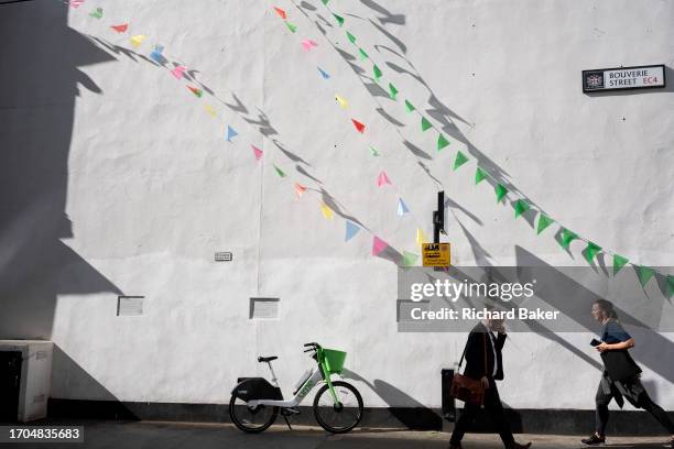 Members of the public walk beneath triangular bunting in Bouverie Street in the City of London, the capital's financial district, on 3rd October...