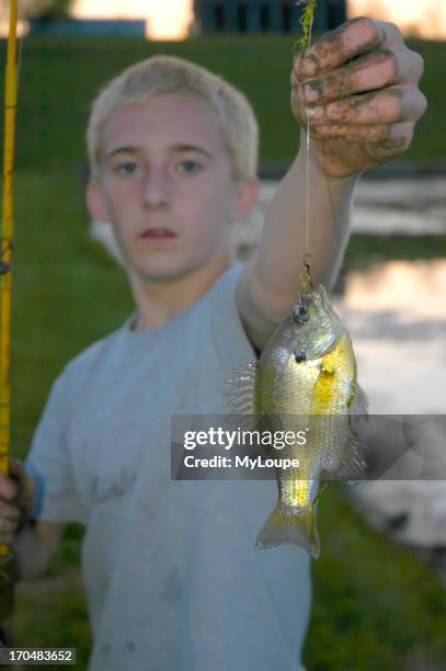 Teenage boy showing off his catch of a Bluegill fish from a rural farm pond at sunset on a early Spring evening.
