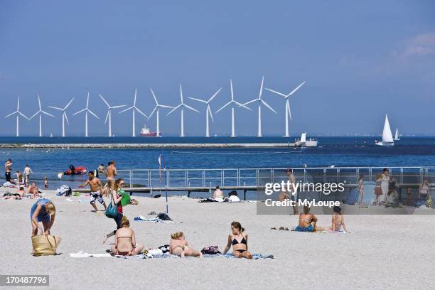 People on the beach at Strandpark, Amager, Copenhagen, Denmark with wind turbines in foreground.