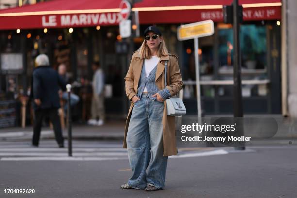 Sonia Lyson is seen wearing a black cap from Yves Saint Laurent x New Era with YSL monogram, sunglasses with golden frame from Celine, a beige long...