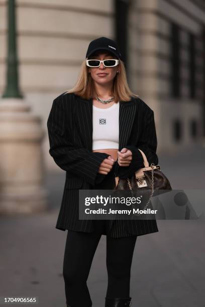 Sonia Lyson is seen wearing a black cap from Yves Saint Laurent x New Era, narrow sunglasses with white frame from Linda Farrow, a twisted silver...