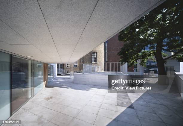 View from under cantilever showing entrance, tree protruding through walkway, granite cladding and surrounding buildings, Parson's Building...