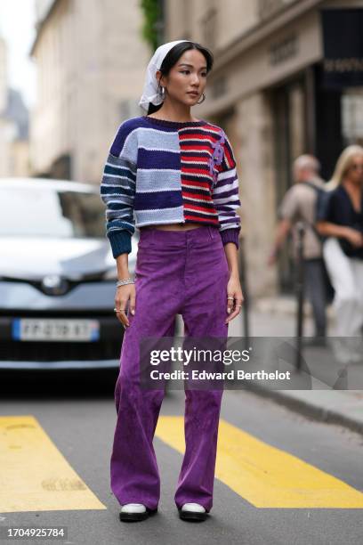 Yoyo Cao wears a white scarf over the head, earrings, a purple and blue and red striped pullover, purple velvet flared pants, outside Cecilie...