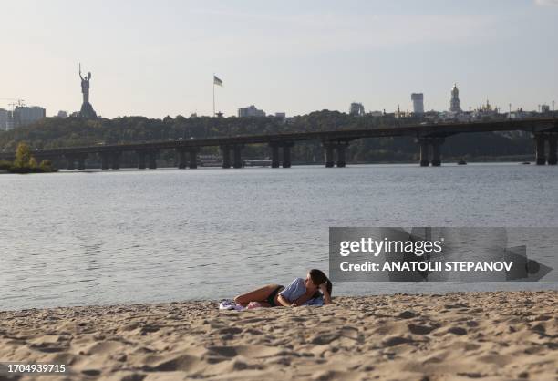 Woman lies on the beach next to the Dnieper river with the Motherland Monument in the background in the Ukrainian capital of Kyiv on October 3, 2023.