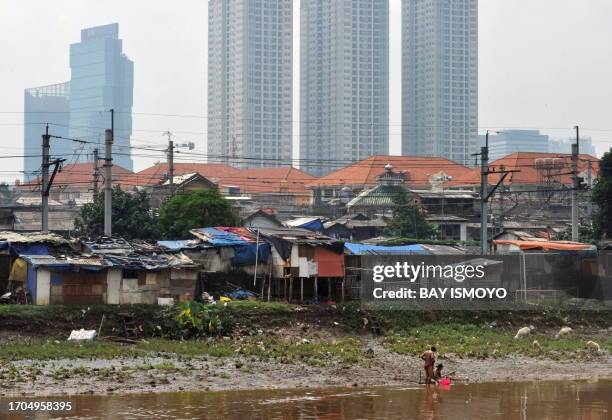 By Jerome RIVET A couple bathes at the riverbank as Jakarta's huts and skylines are seen in the background on September 22, 2010. It has been the...