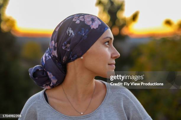 hopeful and confident woman with cancer watching sunset - head scarf stock pictures, royalty-free photos & images