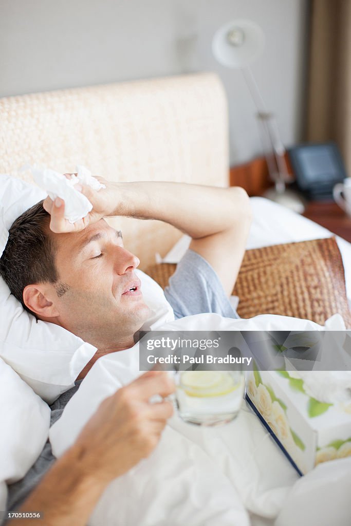 Man sick in bed drinking hot drink