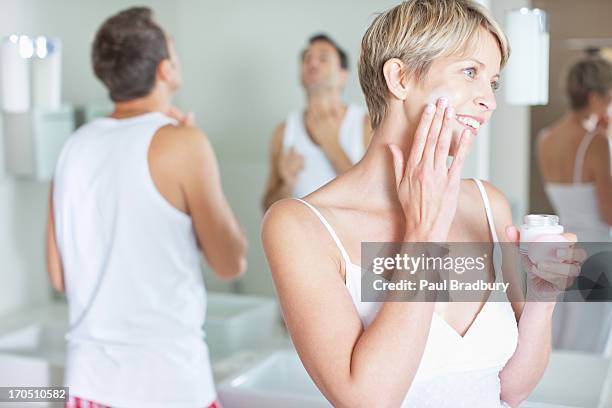 woman applying face cream in the morning - koppel toilet stockfoto's en -beelden