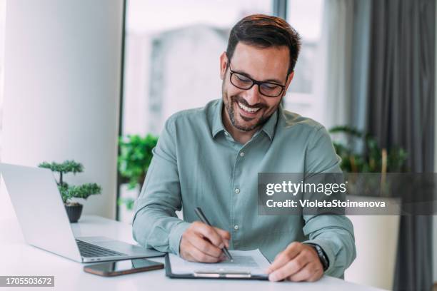 exitoso hombre de negocios en la oficina moderna que trabaja en una computadora portátil y firma un contrato. - llenar el formulario fotografías e imágenes de stock