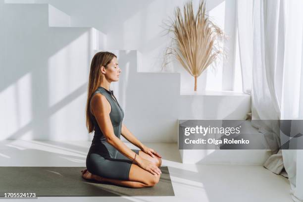 sportive morning mindfulness at home: blonde woman meditates on exercise mat in bright room with legs bent - classe di yoga foto e immagini stock