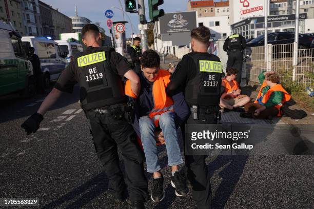 Police remove a climate activist from the group "Last Generation" who was among seven who had glued themselves on the asphalt to block an...