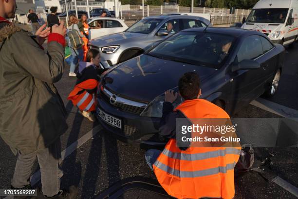 Motorist drives past activists from the group "Last Generation" who were about to block an intersection on an offramp of the A100 highway on...