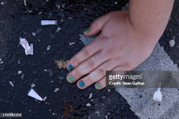 An activist from the group "Last Generation" sits with a hand glued to the asphalt to block an intersection on an offramp of the A100 highway on...