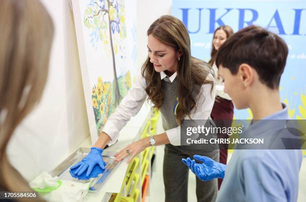 Britain's Catherine, Princess of Wales wearing a Ukrainian ribbon, uses a blue protective glove to make a hand-print on a painting, at an arts and...