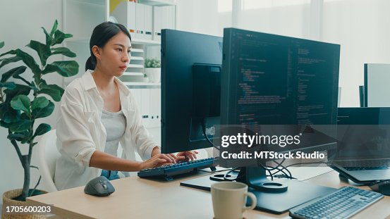 Young Asian woman software developers using computer to write code sitting at desk with multiple screens work at office. Programmer development. Young Asian woman software developers using computer to write code sitting at desk with multiple screens work at office. Programmer development.