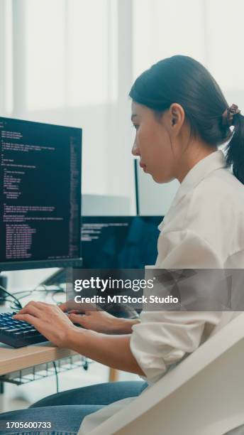 young asian woman software developers using computer to write code sitting at desk with multiple screens work at office. programmer development. vertical screen. - webdesigner stockfoto's en -beelden
